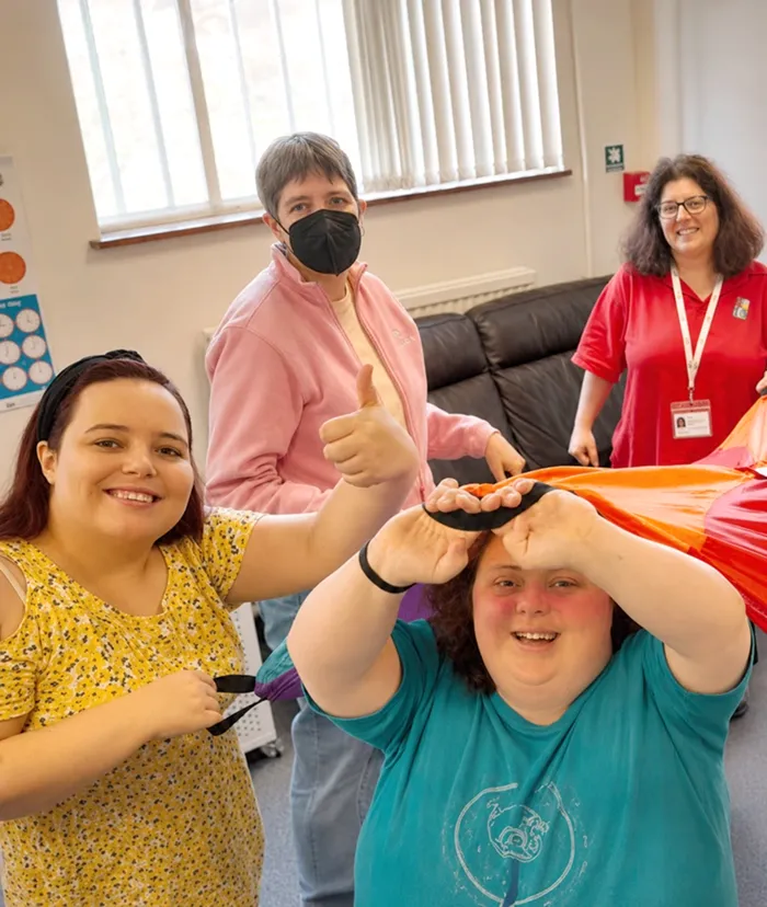 A group of people are smiling and holding up a rainbow parachute