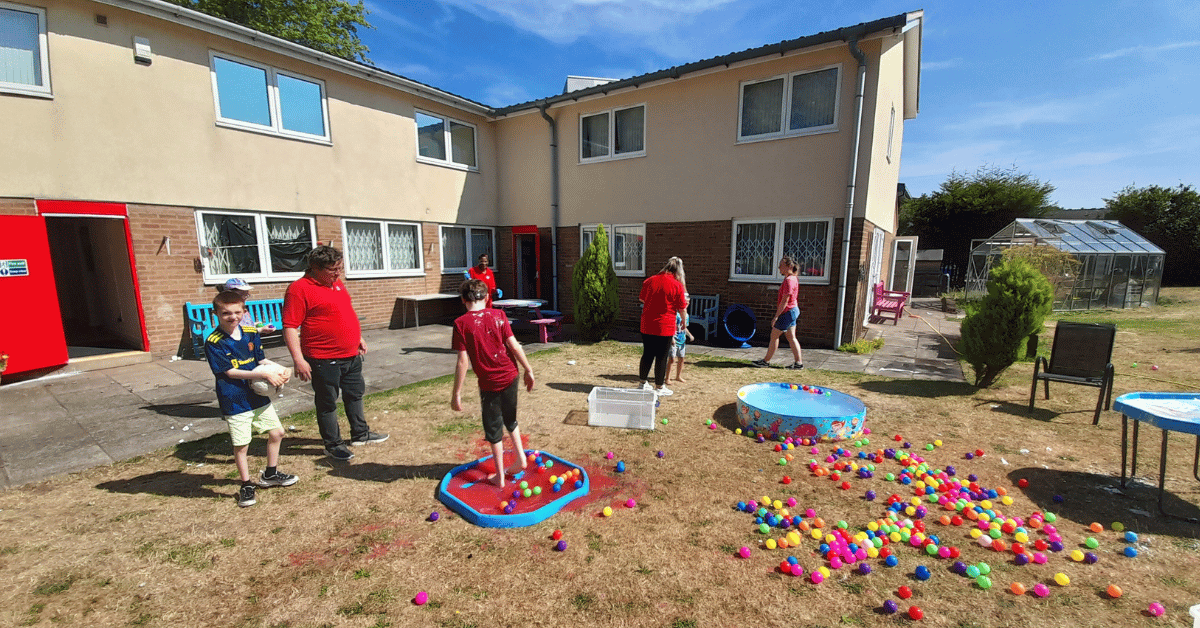 A group of staff and children are playing with water and ball pits outside in a garden.