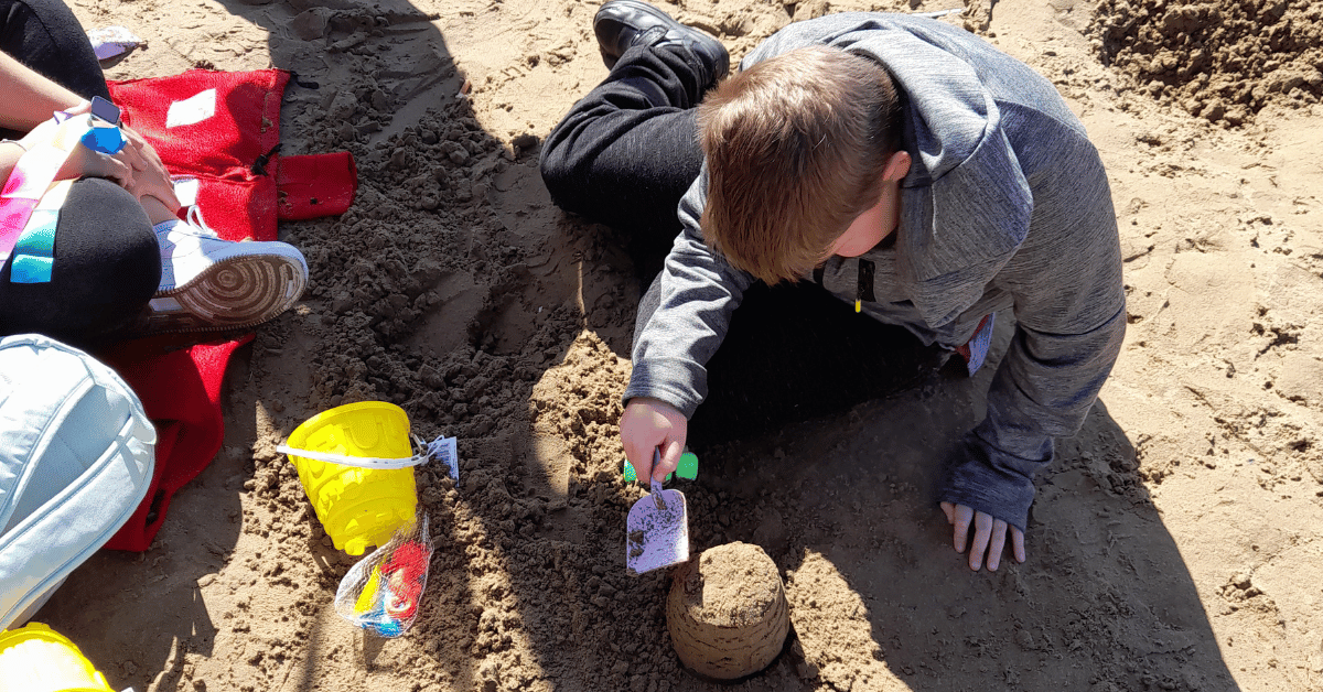 A boy is playing in the sand with a spade and bucket.
