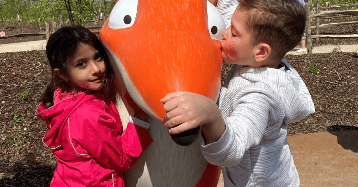 Two children are hugging a giant squirrel statue at the zoo.