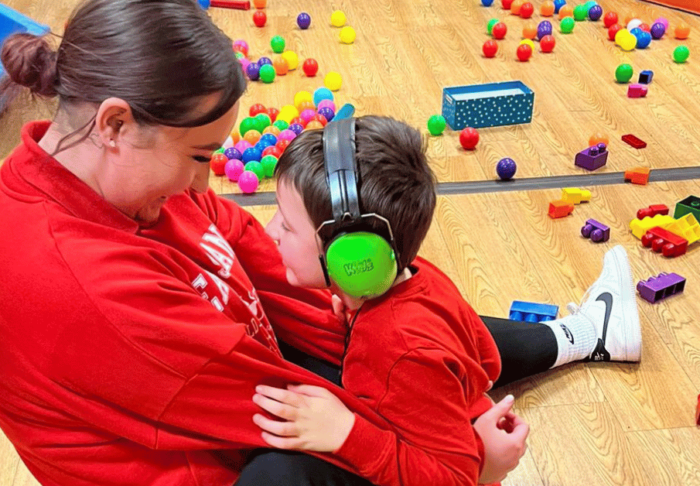 A SoLO staff member and child are sitting on the floor smiling and hugging, surrounded by toys