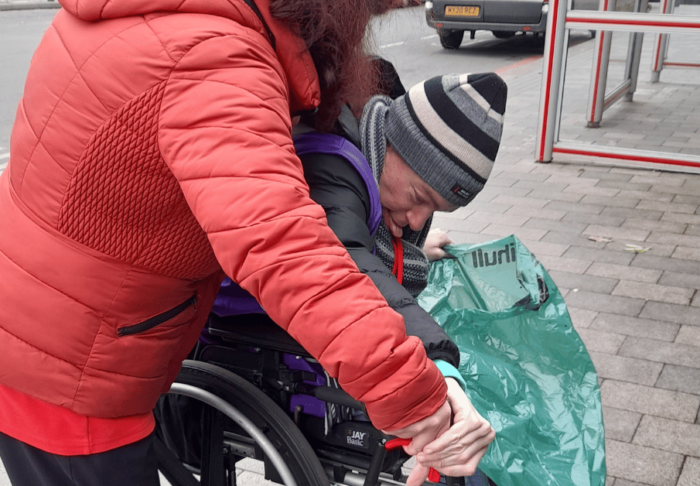 A woman is helping a man in a wheelchair with litter picking