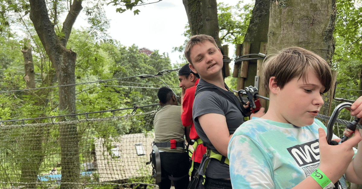 A group of young people are attached to safety lines and climbing a tree top adventure playground
