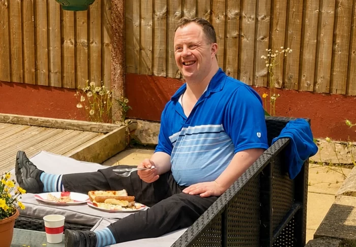 Man sitting in on garden sofa eating a BBQ meal