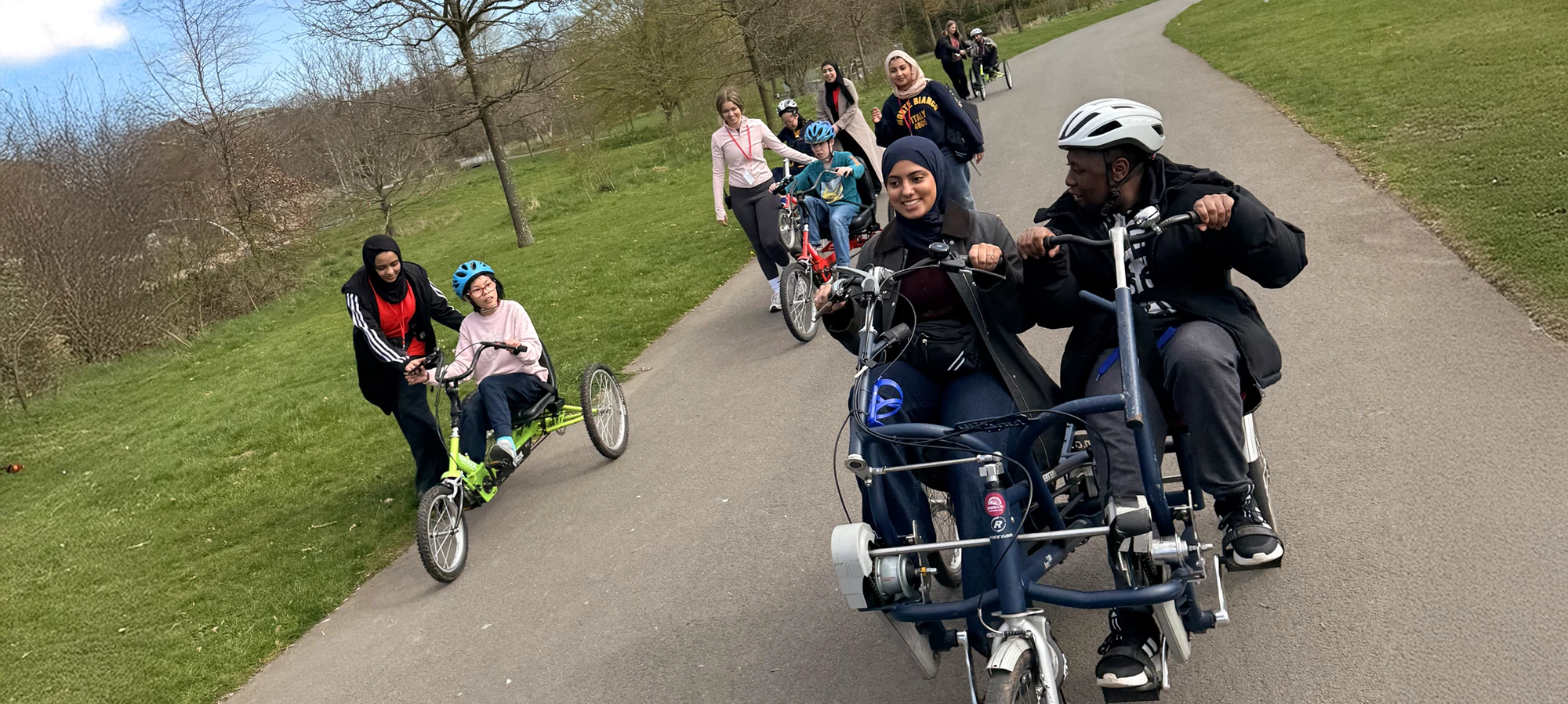 People riding trikes through a park on a sunny day