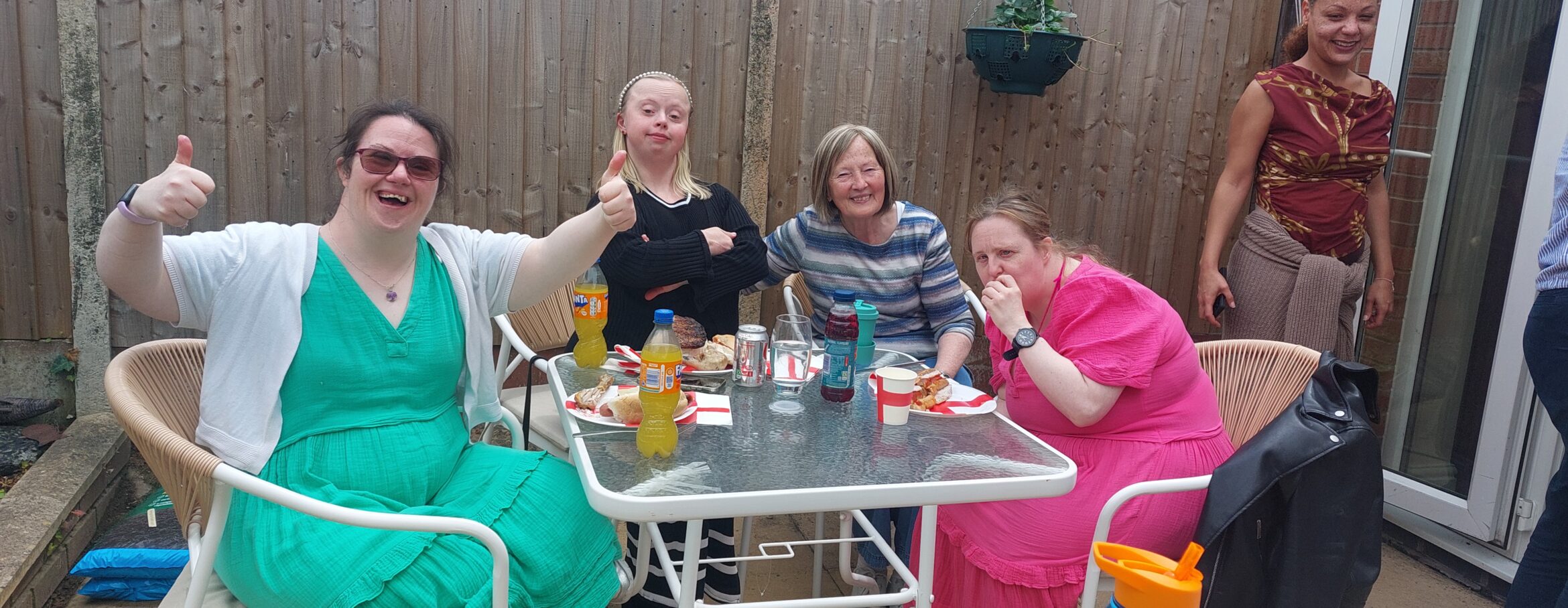 A group of service users smiling at the camera whilst enjoying a BBQ lunch.