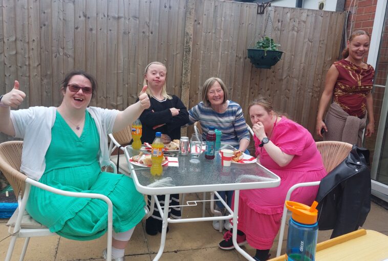 A group of service users smiling at the camera whilst enjoying a BBQ lunch.